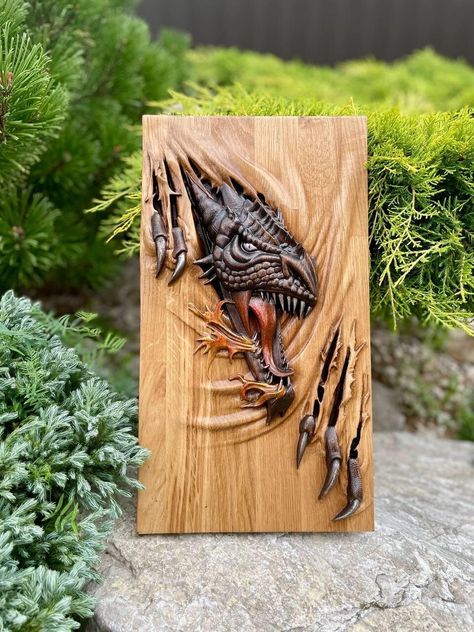 A wooden painting depicting a dragon is a true work of art that combines the natural beauty of wood with the craftsmanship of carving. The painting is made from high-quality wood, carefully treated and polished to create a smooth surface. It features a dragon -- a mythological creature symbolizing strength, wisdom, and protection. The carving impresses with its detail: each scale on the dragon's body, its sharp claws, and expressive face create a sense of realism and dynamism. The background of the painting is also decorated with carved elements, adding depth and volume to the composition. The dragon breaks through the base of the image with its claws, making the painting even more realistic. The dragon's eyes are meticulously carved from wood, appearing lifelike and adding even more expre Cargo Ideas, Dinosaur Wood Carving, Wood Dragon Art, Dragon Faces, Fantasy Wood Carving, Viking Wood Carving, Unique Wood Carving, Wood Carved Dragon, Wooden Dragon