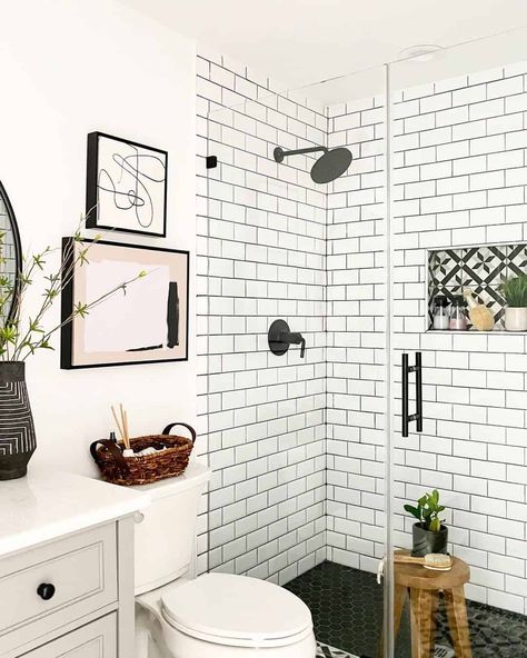 White subway tile shower is finished with a black faucet kit and seamless glass enclosure. A wooden stool is placed in the shower on top of black hexagon floor tiles. Black Hexagon Tile Shower, Black Tile Bathroom, White Tiles Black Grout, Black Hexagon Floor, Hexagon Tile Bathroom Floor, Mosaic Tile Bathroom Floor, White Subway Tile Shower, Half Wall Shower, Bathroom Shower Floor