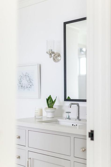 A light gray bath vanity adorned with chrome hardware is topped with an off-white quartz countertop holding a chrome faucet kit beneath a black vanity mirror lit by chrome and clear glass sconces. Black And Chrome Bathroom, Black Vanity Mirror, Inset Drawers, Brick Bathroom, Chrome Bathroom Hardware, Top Bathroom Design, Quartz Backsplash, Bathroom Faucets Chrome, Wooden Bath