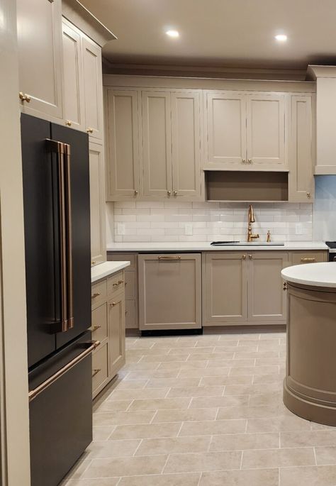 Shown here, a medium-toned mushroom (greige-beige-taupe) kitchen with painted cabinets, travertine-look tile floor, subway tile backsplash and white quartz countertop with GE Cafe Matte Black appliances, fridge has brushed brass hardware. Gold faucet.   #kyliem #kitchenremodel #paintedcabinets #diy #homeupdate Mushroom Grey Kitchen Cabinets, Gray Cabinets White Subway Tile, Small Kitchen Taupe Cabinets, Tan Beige Kitchen Cabinets, Kitchen Cabinet Colors With White Quartz, Neutral Kitchen With Granite, Oak And Taupe Kitchen, Greige Cabinets Gold Hardware, Beige Kitchen Gold Hardware