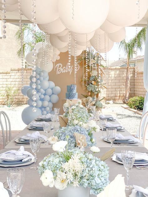 Event Du Jour flawlessly executed this blue and white baby shower. Pearl details cascaded from the balloon arrangement suspended above the table topped with arrangements of blue hydrangeas and white peonies. Unique charger plates and textured glassware furthered the picture-perfect tablescape. Bapstim Decorations, Neutral Blue Baby Shower Ideas, Boys Christening Ideas, April Boy Baby Shower Ideas, Spring Boy Baby Shower Themes, Luxury Baby Shower Ideas Boy, Outdoor Babyshowers, Classy Boy Baby Shower Ideas, Bris Decor