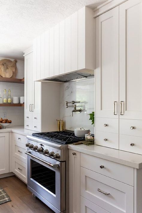 White shaker cabinets with polished nickel hardware flank a stainless steel oven range placed against a marble slab backsplash under a stain nickel swing arm pot filler mounted beneath a shiplap hood. Kitchen Hoods, Kitchen Corner, Kitchen Stove, Farmhouse Style Kitchen, Trendy Kitchen, Black Kitchens, Kitchen Tiles, Range Hood, Ideas Kitchen