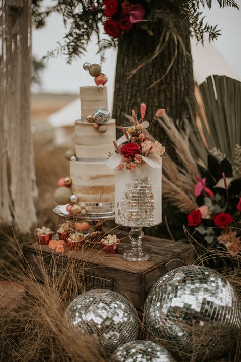 This shows images of a cake display at an outdoor wedding. There are two cakes, one three-tiered cake and a single layer cake, both on glass vintage cake stands. The cakes are displayed on a crate. At the base of the crate are differently sized silver disco balls. Behind the cake display are dried flower arrangements. Pampas Disco Wedding, Boho Disco Wedding Cake, Groovy Wedding Cake, Disco Cowboy Wedding, Disco Ball Wedding Cake, Disco Wedding Cake, Bundt Cake Wedding, Disco Ball Wedding Decor, Disco Ball Cake