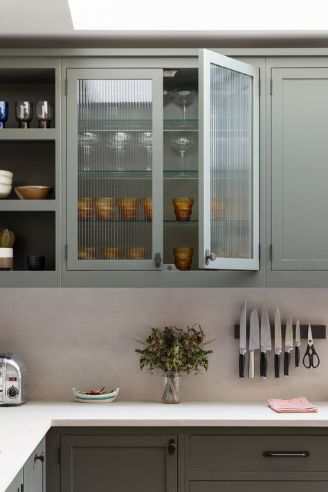 This kitchen showcases a wall cabinet with fluted glass doors, adding a touch of elegance and texture. The cabinet, painted in Little Greene's Pompeian Ash, provides a glimpse of neatly arranged glassware inside. The sleek handles are from Corston (Kilburn Furniture Knob and Kilburn Furniture Handle). Shaker Glass Cabinet Doors, Glass Panel Kitchen Cabinets, Fluted Glass Cabinets Kitchen, Fluted Glass Door Kitchen Cabinets, Glass Door Kitchen Cabinets, Fluted Glass Kitchen, Pompeian Ash, Fluted Glass Cabinet, Kitchen With Dark Cabinets