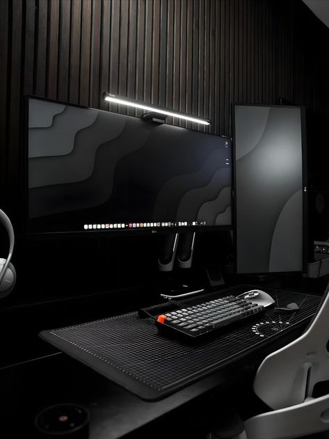 A contemporary and sophisticated workspace featuring a minimalist black desk setup with multiple monitors. The room is highlighted by vertical wooden slats on the wall and a sleek LED light strip above the main monitor, adding a modern touch to the space. The desk is equipped with a high-end mechanical keyboard, a precision mouse, and neatly arranged tech accessories, all complemented by ambient lighting to enhance the dark, chic aesthetic. Aesthetic Desk Setup, Small Room Setup, Minimal Desk Setup, Minimal Workspace, Minimal Desk, Gaming Desk Setup, Aesthetic Desk, Desk Setups, Home Studio Setup