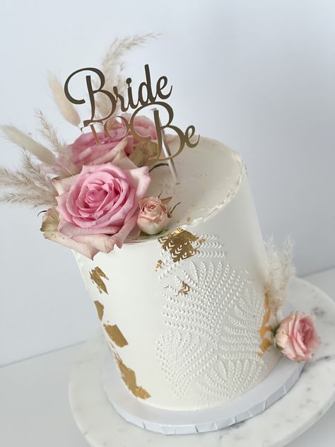 Tall white cake with gold leaf. White stencil pattern over the cake. The top and side is decorated with pink roses and dried florals. A matte gold topper reads “Bride to be” Two Tier Bridal Shower Cake, Cake Stencils Buttercream, White Bridal Shower Cake, Floral Bridal Shower Cake, Stencil Wedding Cake, 1 Tier Wedding Cakes, Wedding Cookies Decorated, Wedding Stencils, Floral Cake Design