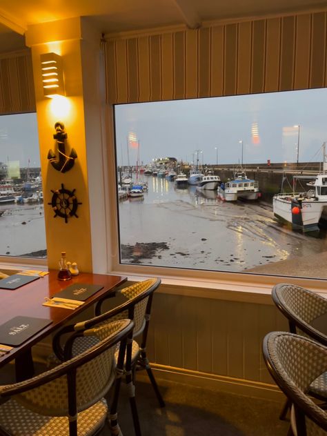 Image shows a dimly lit restaurant. Outside of the window is a marina view. Fish And Chips Restaurant Design, Seafood Restaurant Aesthetic, Fish And Chips Restaurant Interior, Restaurant With Sea View, Marina Restaurant, Fish And Chips, Restaurant