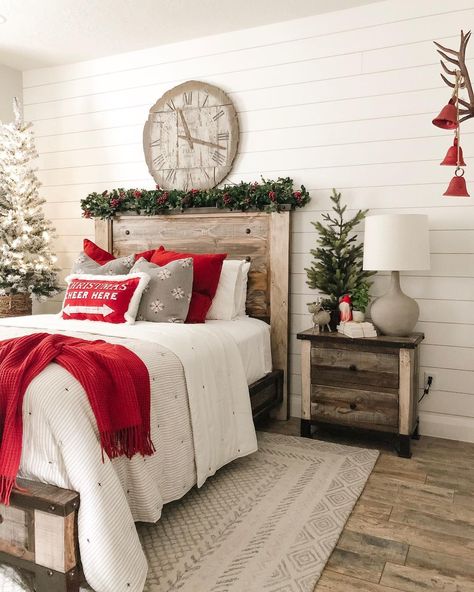 This bedroom boasts white shiplap walls and a warm wood floor. A garland with red berries is laid on the wooden headboard of the bed. A lit Christmas tree sits in the corner. Red and grey pillows decorate the white bedding. A red throw blanket is tossed on the corner of the bed that rests on a beige area rug. Bedroom With Shiplap, White Shiplap Walls, Shiplap Headboard, White Bedside Lamps, Light Blue Bedding, Christmas Bedroom Decor Ideas, Lit Christmas Tree, White Quilt Cover, Christmas Bedroom Decor