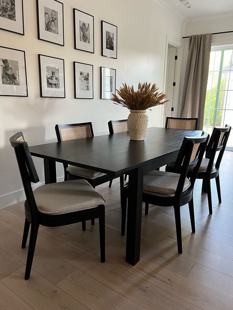 Black table with 6 chairs around it. The chairs have a black base and weaving on the back with cream cushions.