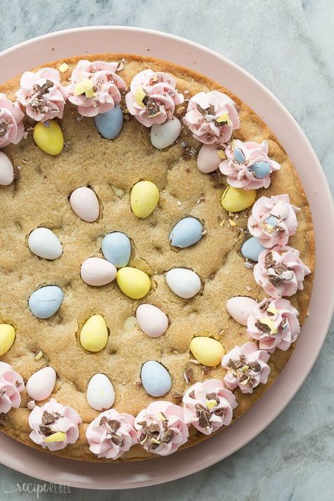 This Easter Mini Egg Cookie Cake is a fun twist on Easter dessert! A soft, chewy, cookie cake, loaded with everyone's favourite candy -- Mini Eggs! -- and garnished with swirls of pastel buttercream, this easy dessert is a showstopper for sure! Includes step by step recipe video. Mini Egg Cookie Pie, Mini Easter Desserts, Spring Sweets, Easter Cookie Cake, Mini Eggs Cookies, Easy Puddings, Easter Snacks, Dessert Recipes For Kids, Holiday Sweets