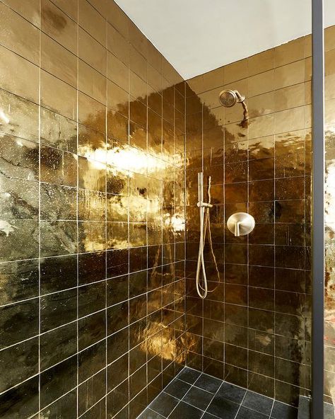 A brushed gold shower head is mounted to shiny gold grid shower wall tiles over black grid floor tiles. Gold Tiles Bathroom, Amber Interiors Bathroom, Golden Bathroom, Gold Tiles, Black And Gold Bathroom, Gold Floor, Shower Wall Tile, Gold Tile, Gold Mosaic