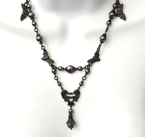 Black and Purple Pearl Victorian bat necklace Vampress Iridescent Purple peal and Black Necklace Halloween Necklace Bat Necklace. This is definitely a statement necklace! Featuring very rare Tierracast black pewter hardware including the black bat charms and beautiful bead caps!  The gorgeous Swarovski Iridescent purple pearls look so cool with the matt black hardware! The necklace is loaded with these fantastic Swarovski Iridescent purple pearls! The center pearl is a rare coin purple with various sized swar pearls connecting the delicate black figaro chain. The black brass heart shaped connector has a lovely victorian design and from it drops more pearls with the bottom pearl surrounded by a black Victorian bead cap. The chain is a delicate figaro with a lobster claw clasp and 2 inch ext Black And Purple Necklace, Pewter Hardware, Purple Gothic, Bat Necklace, Rockstar Gf, Iridescent Purple, Halloween Necklace, Clothing Pieces, Handmade Jewelry Tutorials