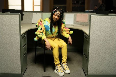 Stephanie Hsu sits in a grey office cubicle in a desk chair. She sports yellow latex pants, platform sneakers, and a colorful jacket made of stuffed animals. Her black hair is pinned out of her face with decora style plastic clips. She has a curl of hair gelled artfully across her forehead. Jobu Tupaki, Stephanie Hsu, Joy Costume, Elizabethan Ruff, White Long Gown, Everything Everywhere All At Once, Braided Hairdo, Argyle Sweater Vest, Good For Her