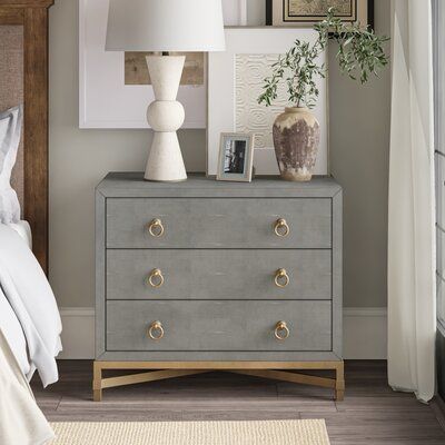 This nightstand provides you with tons of room to store your bedtime necessities and add plenty of glam style to your bedroom. It's crafted from engineered wood with a neutral stone-like coating that works with a variety of color schemes. The upper compartment rests on a sleek gold-finished metal frame with matching crossbar supports and ring pulls on each of the three drawers. The drawers give you a spot to keep linens and other essentials organized and in one place. Measuring 35" wide, this be Brushed Gold Ring, Gray Nightstand, Nightstand Wood, Metal Nightstand, Ring Pulls, Style Nightstand, 3 Drawer Nightstand, Gold Bedroom, White Nightstand