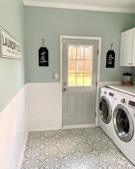 Gray door is fitted into a light green wall with white beadboard wainscoting. A white washer and dryer are placed next to the door in this laundry room featuring white and gray mosaic flooring. Seafoam Green Laundry Room, Soft Green Laundry Room, Eucalyptus Laundry Room, Laundry Room Gray Walls, White Cabinets In Laundry Room, Pale Pink Laundry Room, Laundry Room With Beadboard, Tile Wall In Laundry Room, White Tile Green Wall Bathroom