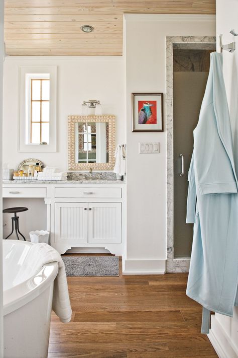 White walls, white cabinets, and neutral marble countertops give a light and airy feel to this bath. Wood floors and a light-stained plank ceiling aren’t so dark as to make the space feel closed in. #bathroomdecor #bathroomdesign #bathroomideas #whitebathroom #southernliving Calming Bathroom, Bathroom Cabinet Colors, Southern Living Idea House, Cabinet Inspiration, Bath Makeover, Serene Bathroom, Bathroom Retreat, Georgia Homes, Beach Cottage Style