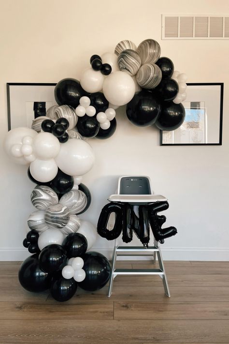 Cake smash setup with high chair in front and a balloon garland arched over the top of the chair and cascading down to the floor on the left hand side.  Balloons are black, white, and black / white marble of varying sizes, and there are balloons on the front of the high chair that read "ONE" in black. Black And White First Birthday, Party Animal Birthday, First Birthday Cake Smash, 1st Birthday Themes, One Balloon, First Birthday Cake, 1 Birthday, Birthday Cake Smash, Party Animal