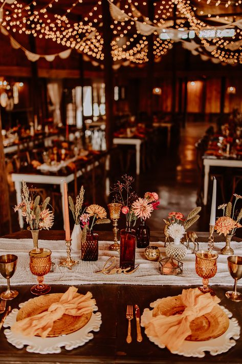 Sweetheart table at Boho styled wedding reception with amber, brass, and milkglass vessels. Amber Glass Wedding Tables, Wedding Tables With Brass Candlesticks, Vintage Table Wedding Decorations, Fall Farm Table Wedding Decor, Boho Vintage Wedding Table, Sweetheart Table Vintage, Brown Glass Wedding Centerpieces, Amber Glass Wedding Table, Brown Table Wedding Decor