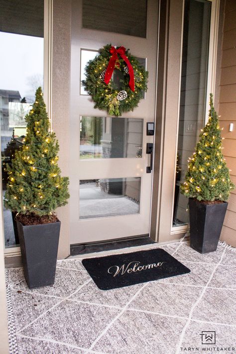 Keep it simple with this Classic Christmas Porch. Featuring layered porch rugs, mini Christmas trees and a fresh green wreath with red bow! Christmas Front Porch Trees, Christmas Tree Planters Front Door, Front Door Christmas Trees In Pots, Entry Door Christmas Decor, Christmas Decoration Front Door, Christmas Decor Ideas Porch, Christmas Entrance Decor, Christmas Decor Front Door, Porch Rugs