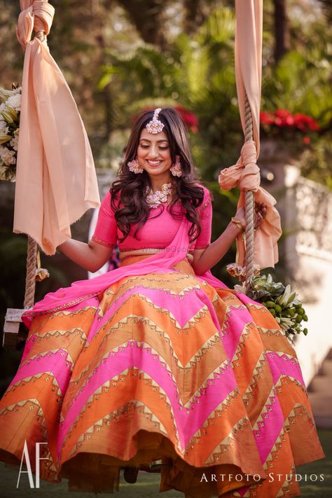 Stunning bright panelled lehenga with a bride on a swing |WedMeGood| Ankita & Ranjit|#wedmegood #indianweddings #mehendi #lehenga #bright #orange #pink #floraljewellery Mehandi Outfit, Mehendi Lehenga, Bridal Lehenga Images, Engagement Board, Mehandi Outfits, Lehenga Images, Bridal Pose, Mehndi Function, Haldi Dress