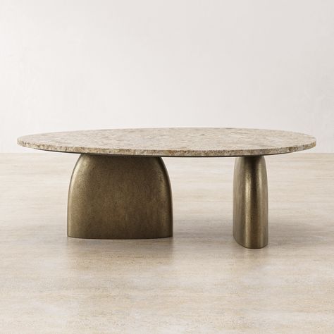 The Matteo coffee table is a testament to sophisticated design, marrying the rugged charm of natural stone with the refined beauty of metalwork. The piece is grounded by two stout legs crafted from aluminum. These legs are finished in an antique brass, giving them a muted glow that speaks of heirloom pieces and understated elegance. Resting upon these metallic supports is a substantial latte travertine top. The travertine, with its natural pits and variations in tone, ranging from creamy whites Tavertine Coffee Table, Stone Table Design, Organic Tables, Voco Hotel, Coffee Table Stone, Organic Coffee Table, Stone Furniture, Classic Coffee Table, African Inspired Decor