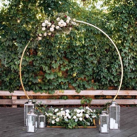 Style your wedding arch in soft and dainty decorative pieces. Use a heavy-duty round gold metal arch and embellish it with cream rose garlands and eucalyptus leaf vines to create an enchanting vibe. You can also adorn more floral garlands and greenery vines at the base of the arch. Spread a few vintage silver metal candle lantern of varying heights to get an ethereal glow as you walk the aisle towards your groom. Arch Decoration Wedding Outdoor Ceremony, Decoration Wedding Outdoor, Outdoor Wedding Setup, Event Decor Ideas, Wedding Outdoor Ceremony, Party Decorations Table, Metal Candle Lanterns, Wedding Arbors, Metal Wedding Arch