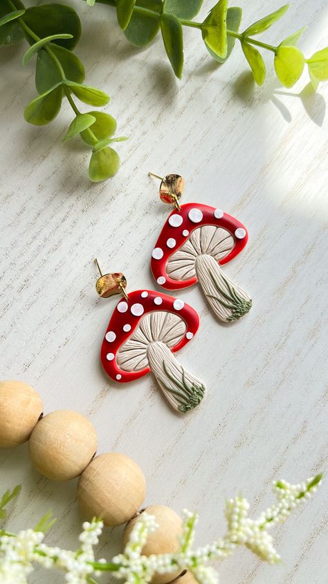 These handmade polymer clay mushroom dangle earrings are perfect for adding a touch of whimsy to any outfit. Each pair is crafted with care to ensure a unique and one-of-a-kind piece of jewelry. The earrings feature cute mushroom designs in red with white spots, dangling from delicate 18K gold plated brass circle. The lightweight design makes them comfortable to wear all day long, and the lead and cadmium free and nickel posts make them safe for most sensitive ears. Wandering Calico Clay earring Cottagecore Earrings Clay, Mushroom Earrings Polymer Clay, Clay Plant Earrings, Mushroom Clay Earrings, Polymer Clay Mushroom Earrings, Clay Mushroom Earrings, Mushroom Designs, Earrings Mushroom, Polymer Clay Mushroom