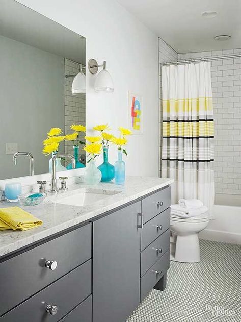 An all-white bathroom gets an energy boost with accents of yellow and gray. Yellow accents sit atop a gray vanity, brightening up the bathroom color scheme. A simple patterned shower curtain emphasizes the shower area and adds a sophisticated dark gray to the mix. Light gray flooring contrasts white walls while looking simple and clean.                         Get this FREE bathroom remodeling guide. Bathroom Colors Blue, Light Grey Flooring, Yellow Grey Bathroom, Best Bathroom Colors, All White Bathroom, Grey Accent Wall, Yellow Bathroom, Gray Vanity, Bathroom Color Schemes