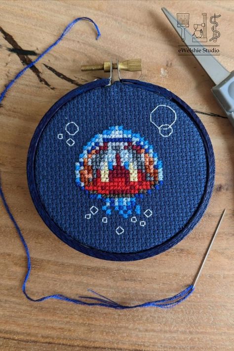 A finished cross stitch of a small jellyfish with red insides on blue cross fabric. Jellyfish Cross Stitch, Small Jellyfish, Floating In The Ocean, Embroidery Floss Crafts, Cute Jellyfish, Blue Jellyfish, Graph Paper Art, Bead Sprite, Types Of Stitches