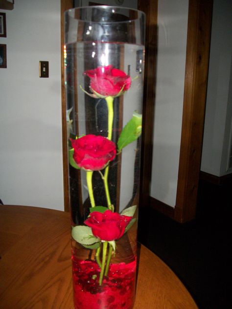 tall cylinder vase w/ red roses submerged in water and red rocks at the bottom of the vase. w/ floating candle to be placed and lit at reception. Submerged Flowers, Candles Centerpieces, Ideas Candles, Tea Lights Wedding, Tall Cylinder Vases, Diy Candle Sticks, Centerpieces Diy, Rose Centerpieces, Diy Roses