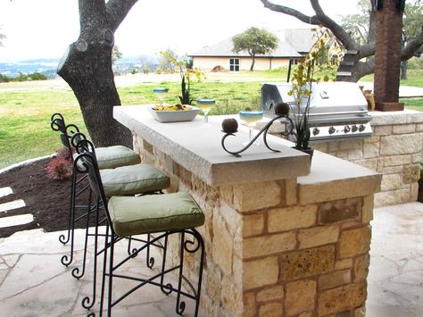 This stone paved outdoor bar features an area for enjoying drinks and entertaining guests. The space is adorned with high chairs with cushion seats and a grill unit. Diy Outdoor Bar, Outdoor Kitchen Countertops, Outdoor Kitchen Bars, Outdoor Kitchen Appliances, Backyard Bar, Diy Outdoor Kitchen, Outdoor Bar Stools, Patio Bar, Perfect Garden