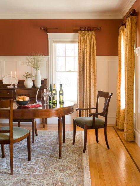 This traditional style dining room features white wainscoting below burnt sienna walls for a bright but earthy feel. Pale yellow curtains continue the warm theme. Victorian Dining Room Decor, Orange Dining Room, Burnt Orange Living Room, Wainscoting Living Room, Black Wainscoting, Wainscoting Kitchen, Wainscoting Bedroom, Dining Room Victorian, Dining Room Wainscoting