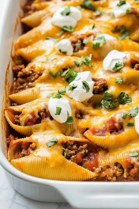 These taco stuffed shells combine tender pasta, seasoned beef, and melty cheese, all topped with zesty enchilada sauce and refreshing sour cream. Taco Stuffed Shells Recipe, Enchilada Stuffed Shells, Mexican Christmas Food, Mexican Stuffed Shells, Taco Shell Recipe, Shell Pasta Recipes, Cheese All, Jumbo Pasta Shells, Shells Recipe