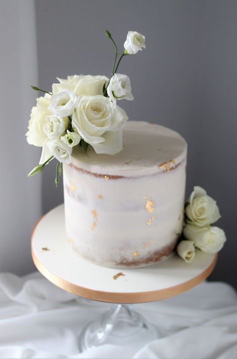 A white one tier semi-naked butttercream wedding cake decorated with cream roses and white lisianthus and flecks of edible gold leaf. Edged in gold ribbon and displayed on a clear glass cake stand. Elegant Intimate Wedding, Wedding Cake With Fresh Flowers, Wedding Cake Simple Elegant, Golden Birthday Cakes, One Tier Cake, White And Gold Wedding Cake, Cake With Fresh Flowers, Gold Leaf Cakes, White Lisianthus