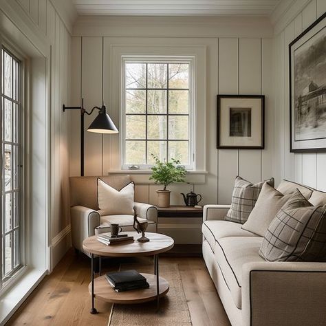 A cozy cottage living room with cream paneled walls, cream sofa, plaid throw pillows, accent chair, round metal and wood coffee table, black English floor lamp, small English cottage living, vintage wall art, and oak wood flooring.   Design: @windthekey  Follow @windthekey for more design inspiration. Cottage Living Room Windows, Built In Sunroom, Living Room New England Style, Apartment Farmhouse Living Room, Small Space Vintage Decor, Cozy Cottage Decor English Country, Modern Cottage Furniture, Cream Cottage Living Room, Small Living Room Sofa And Chair