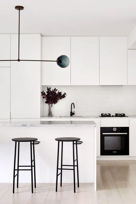 Dull avocado-coloured cupboards that once dominated the kitchen have been swapped for plain white cabinetry, complemented by a white-tile splashback. A slab of pale marble tops the breakfast island. The studio included this so that the inhabitants would have a spot to sit and enjoy meals, dismissing the need for the obtrusive dining table that previously sat in the living room. Winter Architecture, Kitchen Interior Inspiration, White Kitchen Interior, Brighten Room, Painted Brick Walls, Black Window Frames, Black Houses, Architecture Set, White Sideboard