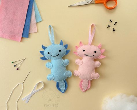 Sew your own Axel & Azul the Axolotls. Fox & Bee's Axolotl felt sewing kits are perfect for kids and adults of all ages and abilities - whether it's your first time sewing or you're an old hand, you'll love making these felt Axolotl decorations. In this kit you have everything you need to make your very own Pink & Blue Axolotls. Approx. Sizes (when made not including the ribbon): 85mm & 135mm each Inside your felt sewing kit * 40% Wool blend felt * Ribbons * Needle & Pins * Brads * Fluffy stuffi Axolotl Decorations, Axolotl Sewing Pattern, Felt Axolotl, First Time Sewing, Felt Sewing Kit, Felt Sewing, Craft Kids, Sewing Kits, Christmas Stocking Fillers