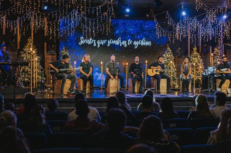 Church Christmas Stage with acoustic worship. Lots of warmth and coziness from warm white christmas lights and edison bulbs. Screen sets the scene and adds colors. They created a sense of intimacy on a big stage by seating all the band members on the wood boxes, cajon height, in a u-shape arrangement. Christmas Stage Decorations, Church Stage Decor, Christmas Stage Design, Church Christmas Decorations, Concert Stage Design, Stage Designs, Christmas Stage, Stage Set Design, Christmas Church