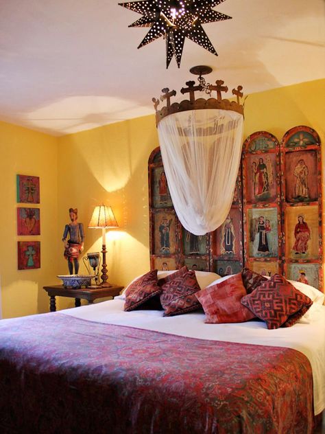 Religious elements prominent in Mexico influence this yellow guest bedroom designed by Carole Meyer. The handmade iron crown holds mosquito netting above the bed and represents wrought-iron details popular in Spanish design elements. The headboard is a hand-painted folding screen mounted to the wall, and the star-shaped tin light fixture brings whimsy to the space. Kilim pillows accent the red paisley bedspread, and the three small paintings on the wall, created by Carole, are inspired by th... Mexican Bedroom Decor, Spanish Style Bedroom, Spanish Bedroom, Style Hacienda, Southwestern Bedroom, Mexican Bedroom, Mexican Style Decor, Mexican Interior Design, Ikea Interior