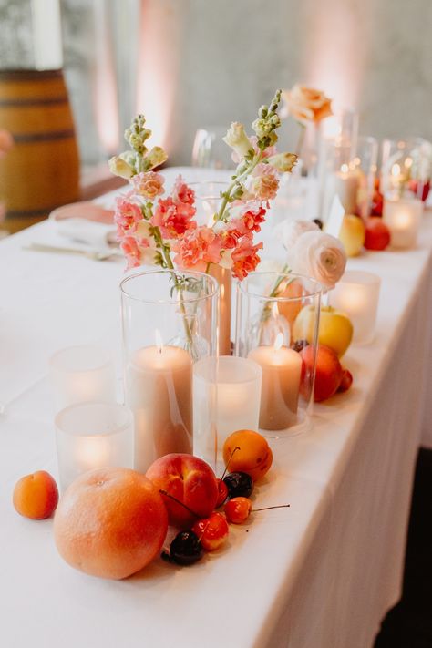 Using the colors of a peach as inspiration, this sweetheart table was filled with neutral colors so the brightness of the fruit and flowers stood out.  Taupe candles, colorful flowers and fruit across the front of the sweetheart table. Fruit Inspired Wedding Decor, Wedding Table With Fruit, Fruit As Wedding Decor, Wedding Centerpieces With Fruit, Fruit Table Decor Wedding, Fruit Wedding Table Decor, Table Decor With Fruit, Fruit Wedding Centerpieces, Peach Table Decor