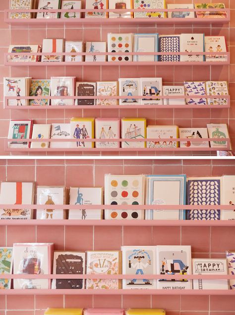 In this modern retail store, this greeting card display is colored the same as the dusty pink tiles, almost blending into the walls. Colorful Boutique, Store Stand, Greeting Card Display, Craft Market Display, Retail Space Design, Stationary Store, Stationary Shop, Craft Stalls, Pink Tiles