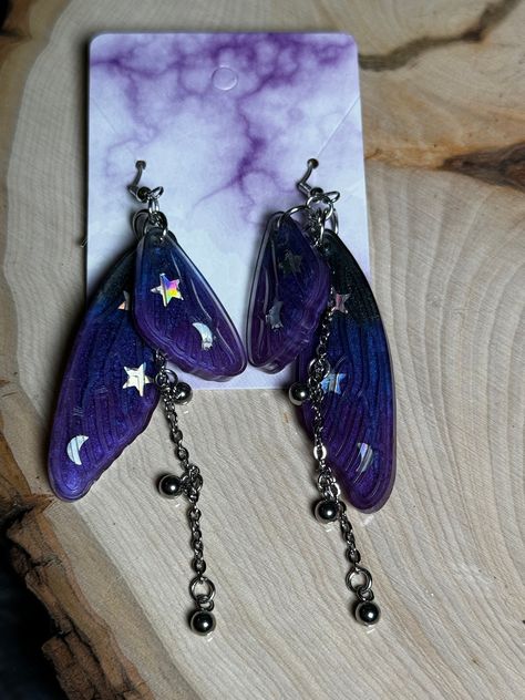 These Dark Purple Magic Chain Double Fairy Wings are amazing earrings for yourself or someone else as a gift! The Earring hooks are made of 925 sterling silver and earring backs are made of clear silicone.  Earrings are handmade which makes every piece a unique piece of art.   Earring size from hook to bottom of chain: 3.5" Fairy Wing Size: 2" (1) Earring Weight: 3.5 oz.   Do not leave in a hot car. Handle with care. BatCravt is not responsible for any damage after shipping.  No returns or exchanges accepted. Emerald Green Accessories, Outfit Ideas Purple, Fairy Wing Earrings, Magic Purple, Car Handle, Amazing Earrings, Purple Magic, Glitzy Glam, Purple Accessories