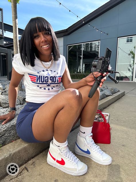 Girl sitting on the ground wearing a white, red, and blue top gun graphic tee, navy biker shorts, a red crossbody bag, and some white, red, and blue Nike blazer mid ‘77 Mini Skirt And Nike Blazers, Graphic Tee And Jordans Outfit, Nike Blazer Mid 77 Outfit Black Woman, Biker Shorts And Sneakers Outfit, Shorts And Sneakers Outfit Black Women, Blazer Shoes Outfits, Nike Biker Shorts Outfit, Shorts And Sneakers Outfit, Blazer Shoes Outfit