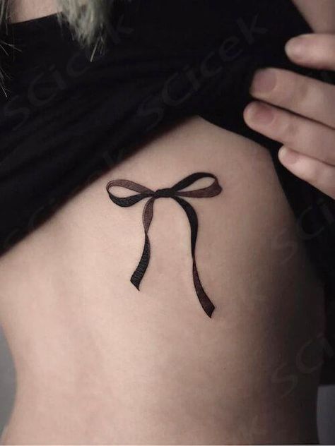 Explore bow tattoo meaning. Discover the symbolic meaning behind bow tattoos and get inspired with our collection of unique bow tattoo designs and bow tattoo ideas. Lace Bows Tattoo, Goth Bow Tattoo, Bow Tattoo Aesthetic, Bow Tie Tattoos For Women, Bow Back Tattoo, Gothic Bow Tattoo, Finger Bow Tattoo, Black Ribbon Tattoo, Black Bow Tattoo