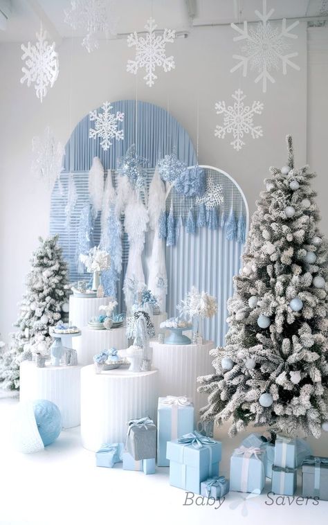 A winter-themed display, perfect for baby shower ideas, features snow-dusted Christmas trees, white snowflakes hanging above, and a collection of blue and silver wrapped gifts. The backdrop includes white and blue decorations, creating a festive yet elegant atmosphere. Winter Wonderland Baby Shower Boy, Unique Baby Shower Ideas, Enchanted Forest Baby Shower, Light Blue Decor, Mannequin Christmas Tree, Unique Baby Shower Themes, Dance Decorations, December Baby, Winter Wonderland Decorations