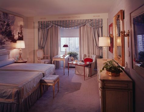 An interior view of an ornate bedroom with two double beds, gilt accented furniture, and a large window with a city view, circa 1980. 80s House Interior, 1980s Living Room, 1980s Bedroom, 80s Living Room, 1980s Interior Design, Bedroom 80s, 1980s Home Decor, 80s Bedroom Decor, 1980s Interior