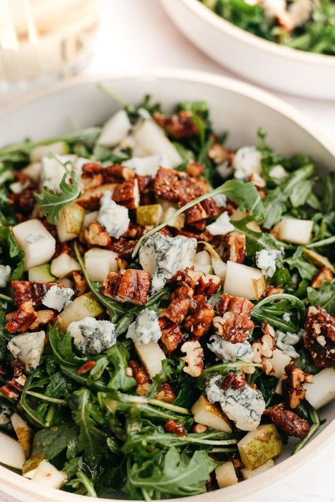 This delicious salad includes peppery arugula, sweet pears, creamy crumbled gorgonzola or blue cheese, and candied pecans. Toss it all in a simple homemade dressing and enjoy! Arugula Salad Thanksgiving, Thanksgiving Salad Arugula, Arugula Blue Cheese Salad, Holiday Arugula Salad, Roasted Pecans For Salad, Pear Prosciutto Salad, Dressed Greens Salad, Gorgonzola Pear Salad, Winter Arugula Salad