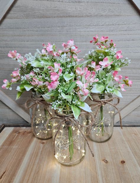 These beautiful faux wildflower and eucalyptus quart size mason jar centerpieces are a Glassy Gal original design. Each centerpiece includes one set of warm white LED fairy lights, a jute bow, and a deluxe faux wildflower and eucalyptus arrangement.  These centerpieces are very popular for weddings, baby showers, parties, corporate events, holiday events, and any other event that requires table centerpieces. They also look great in any room of your house or office. To see other lighted jar options and all of my other listings, please view my shop: https://www.etsy.com/shop/GlassyGalDecor  Each jar set includes: (1) clear quart size mason jar (1) set of LED fairy lights (1) faux wildflower and eucalyptus arrangement  (1) jute bow Dimensions:  Quart jars are approximately 6.25" tall (approxi Fairy Lights In Water Centerpiece, Fairy Birthday Party Centerpieces, Pink And Green Centerpieces, Eucalyptus Arrangement, Jar Centerpiece Wedding, Diy Floral Centerpieces, Romantic Table Decor, Sweet 16 Centerpieces, Pink Mason Jars