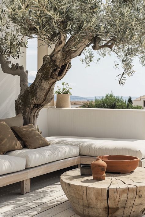 Terrasse extérieure, style méditerranéen, olive centenaire, sofa blanc, coussins couleur taupe, vue sur mer, table basse en bois brut, poterie terre cuite, atmosphère relaxante, design minimaliste, palette de couleurs naturelles, bois clair, coussins confortables, murs blancs, espace ouvert, lumière naturelle, ambiance sereine, éléments organiques, détails rustiques, sol en bois, plante grasse, ciel dégagé, ligne d'horizon, style épuré, textiles luxueux, architecture moderne, intégration naturelle, décoration éco-responsable, finitions de qualité, coin détente. Terrasse Design, Dappled Light, Mediterranean Garden, Outdoor Inspirations, Garden Pool, Interior Garden, Menorca, Terrace Garden, Beautiful Furniture