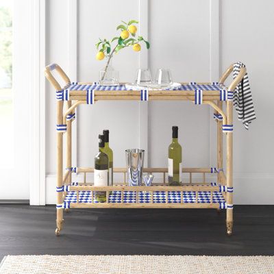 This bar cart offers a stylish way to serve up drinks and snacks, whether you're hosting a gathering or enjoying a relaxing evening at home. The solid bamboo frame features a light brown finish, while the top and bottom shelves showcase woven blue-and-white acrylic detailing for a coastal vibe in your space. With four wheels and two handles, this cart is easy to move around, and the included towel bar ensures you always have a cloth handy for spills. The cart's 50 lbs. weight capacity allows for Coastal Basement, Bar Cart Wood, Rattan Bar Cart, Bar Corner, Wood Bar Cart, Rattan Bar, Serving Cart, Relaxing Evening, Basement Makeover